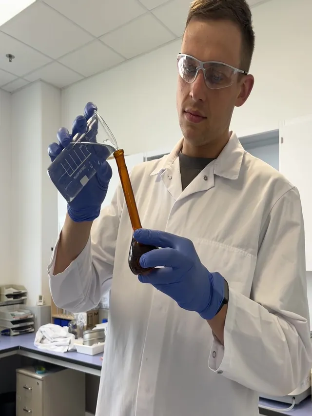 Peter Maibaum im Laborkittel mit Schutzbrille prüft ein Röhrchen