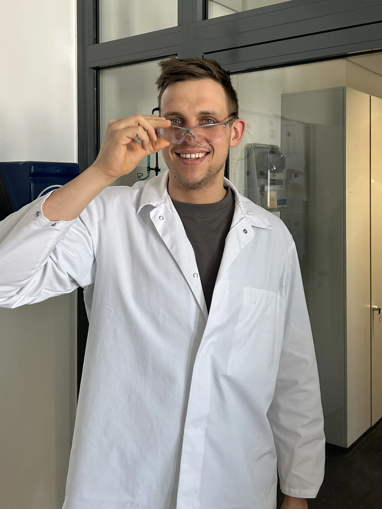Peter Maibaum im Laborkittel rückt lachend seine Schutzbrille zurecht
